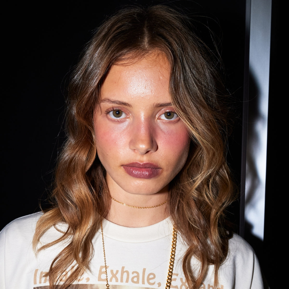 Young woman with wavy hair wears a minimalist gold necklace and a T-shirt. Perfect for luxury jewellery branding or fashion editorial.