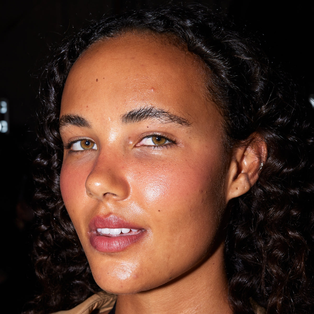Smiling person with curly hair and glowing skin, wearing natural makeup. Ideal for luxury skincare or beauty advertising in Australia.